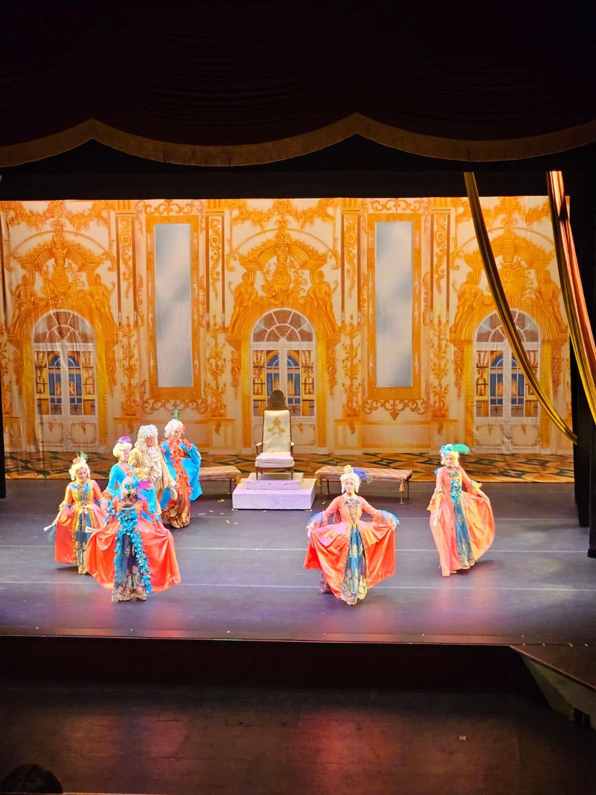 Stage with dancers in colorful costumes performing in front of a golden ornate backdrop.