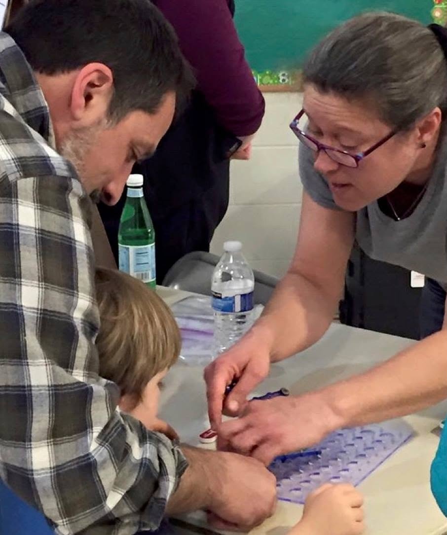 Two adults and a child engaged in an activity at a table with water bottles nearby.