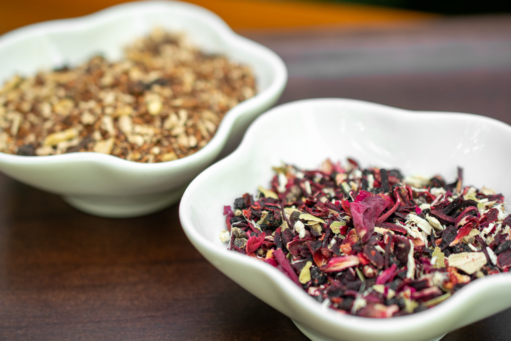 Two white bowls filled with different types of dried herbs or tea leaves on a wooden surface.