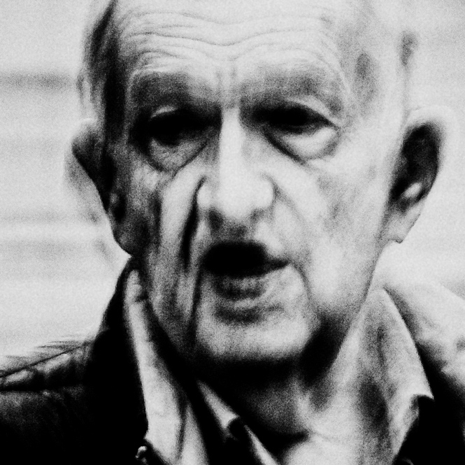 Elderly man with a serious expression, wearing a jacket and shirt, in black and white.