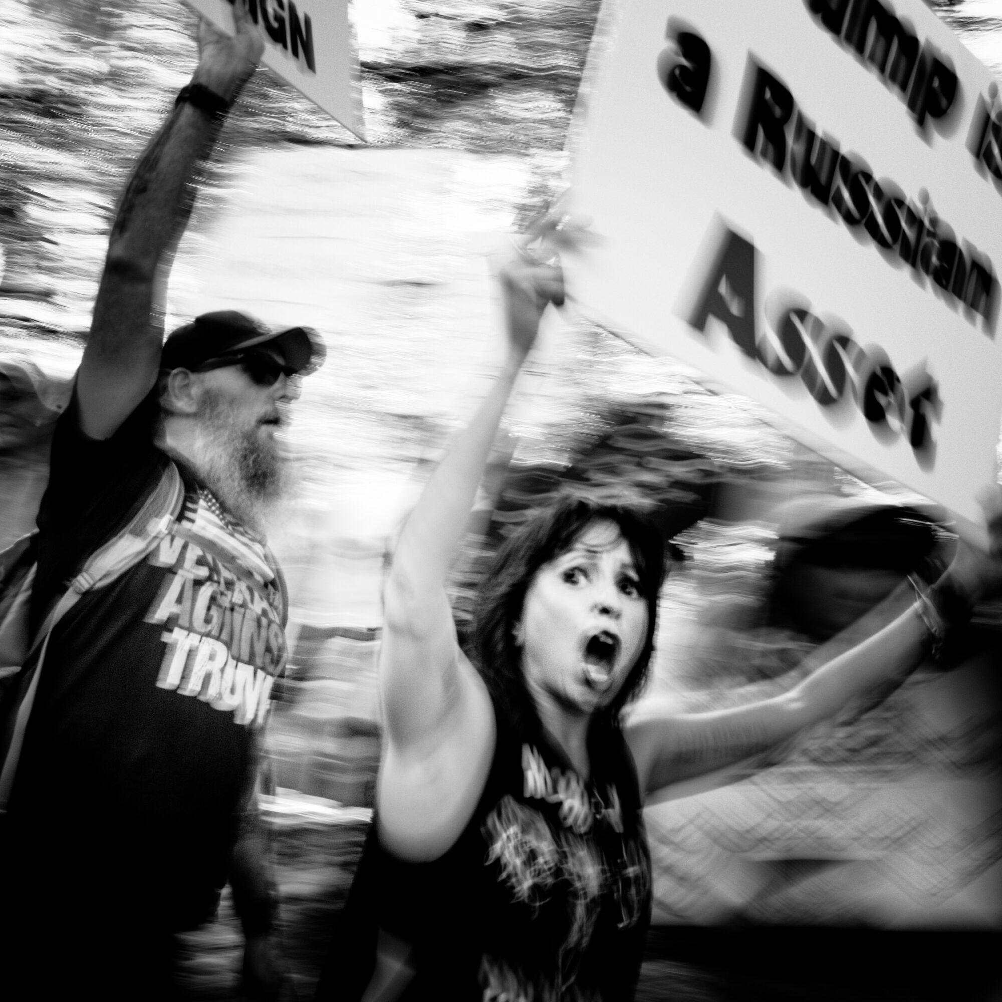 Two people protesting, one woman with arms raised and mouth open, one man holding a sign, in motion blur.