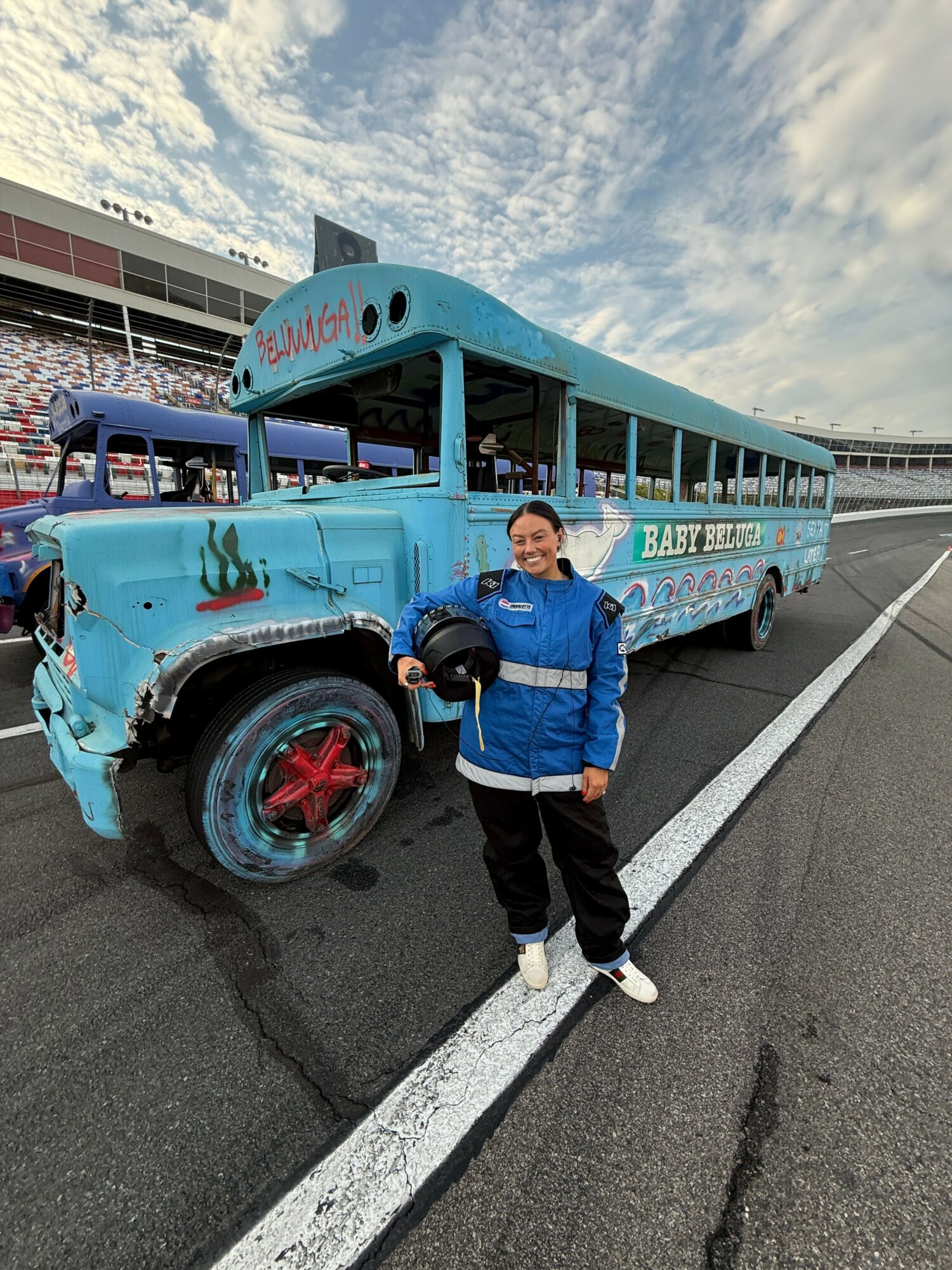 Two children stand next to a blue bus on the side of a road, with a cloudy sky above.