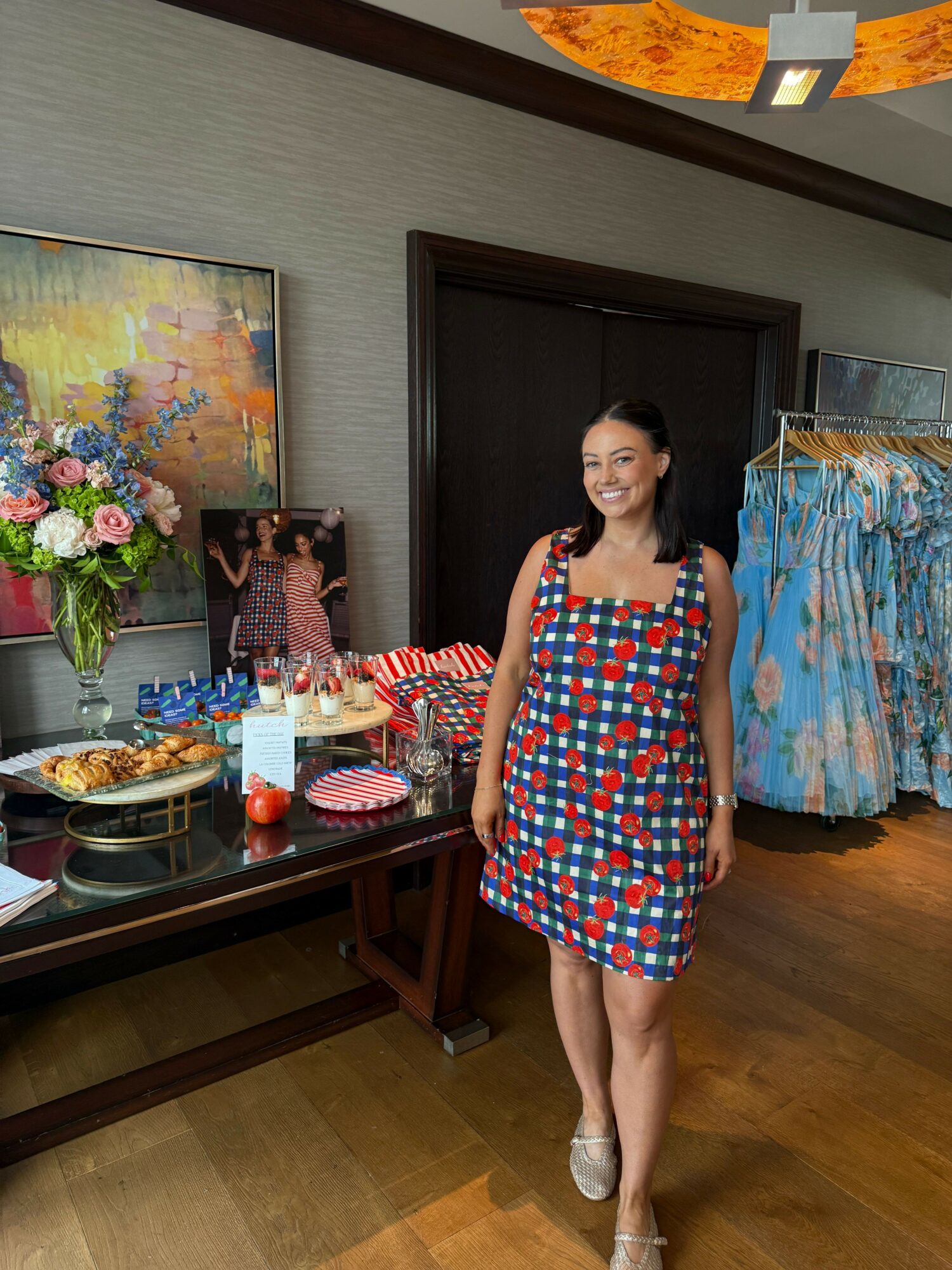Woman in a colorful dress standing in a room with a table of food and decorations, smiling at the camera.