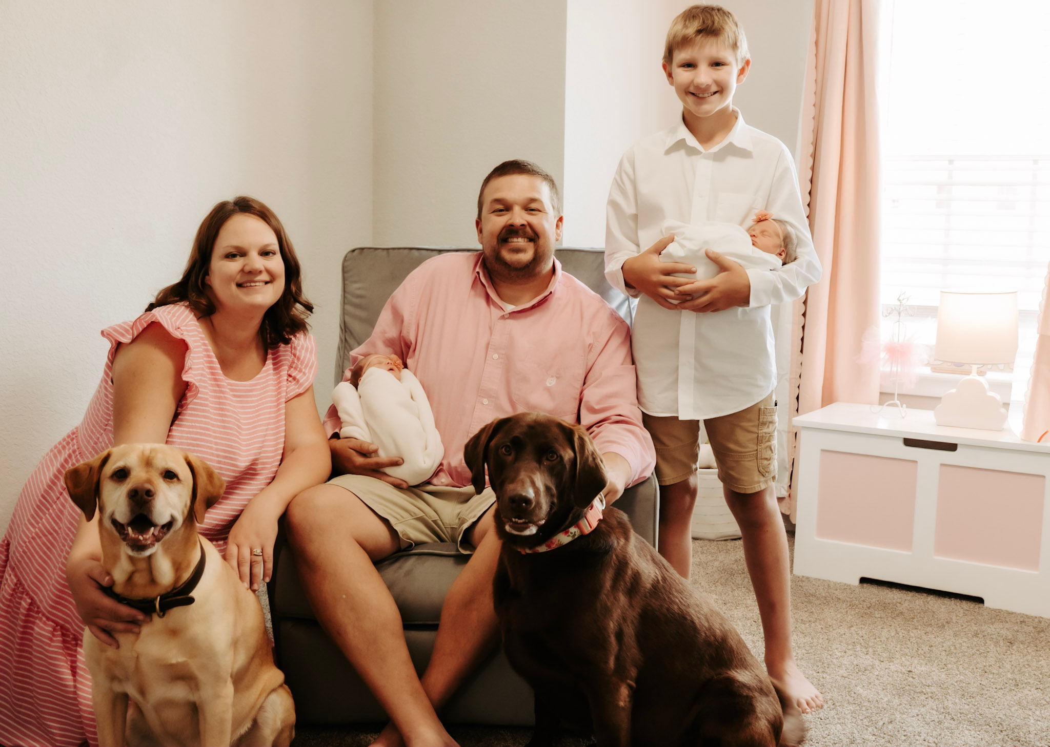 Family with two children and two dogs sitting on a sofa in a bright living room.