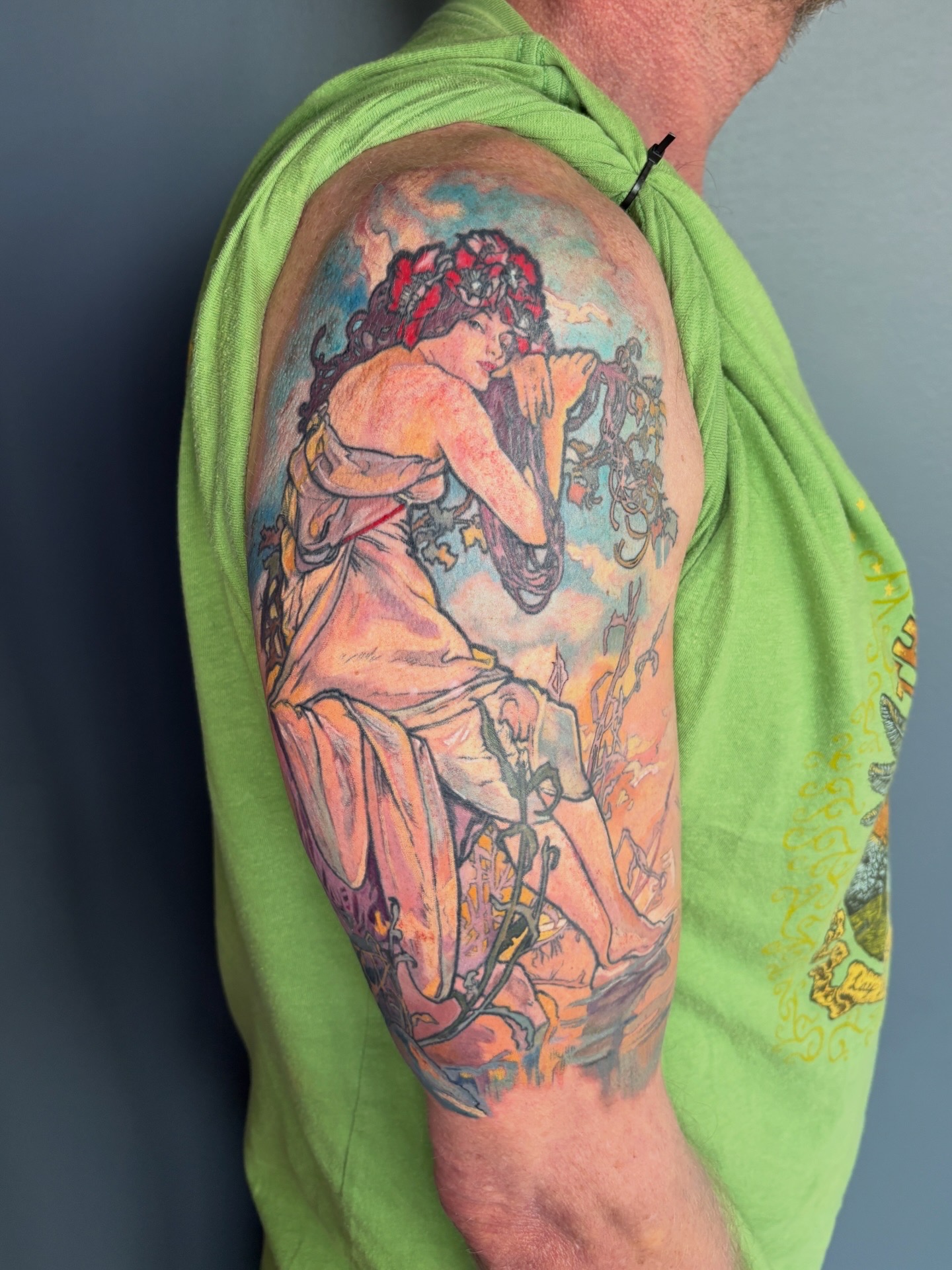Colorful tattoo of a woman with curly hair sitting and playing a musical instrument on upper arm.