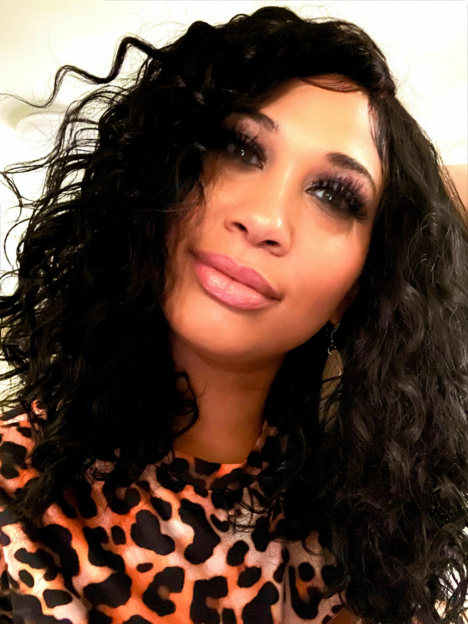 Woman with curly dark hair and makeup, wearing a leopard print top, smiling slightly.